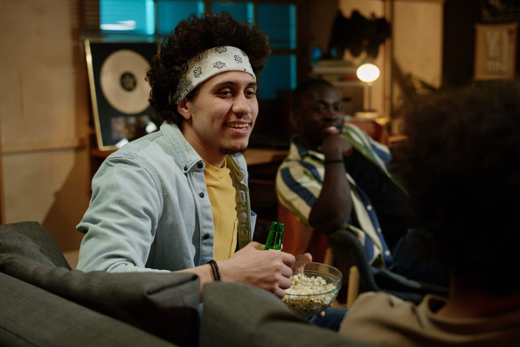 Young man enjoying popcorn and a drink while chatting with friends during a streaming night, reflecting modern social rituals among cannabis users.